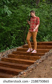 a young man descends the wooden steps in the park holding a phone - Shutterstock ID 2188750865
