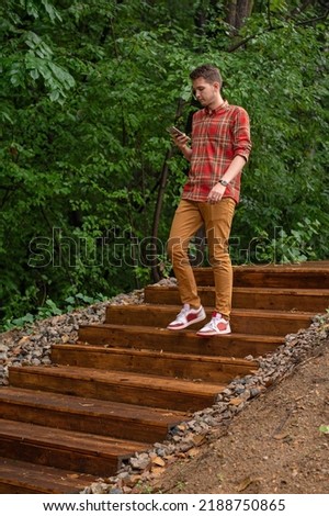 a young man descends the wooden steps in the park holding a phone