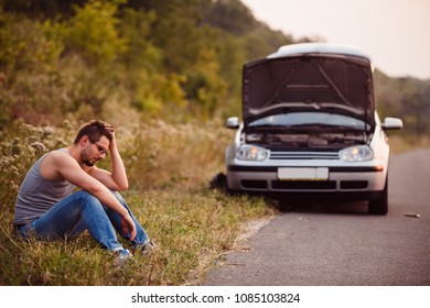 A young man in despair clutched his head, because his car broke down on the road and it is not possible to repair it.