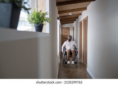 Young Man With Disability In Casualwear Moving Along Corridor Of Modern Apartment While Sitting On Wheelchair