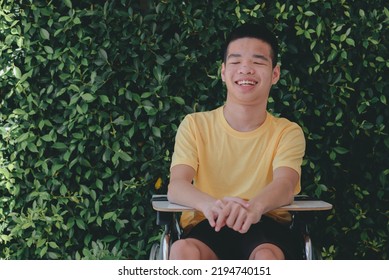 Young Man With Disability With Happy Face In Nature Garden Background Of Home Or Hospital Or School Or Park, Teenager Boy Sitting With Tray For Activities On Wheelchair, Good Mental Health Concept.