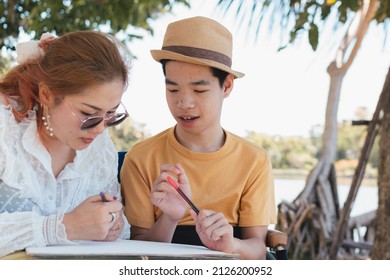 Young Man With Disability And Parent Or Teacher Or Volunteer Or Caregiver Relaxing And Learning Activities With Family At The Outdoor Vacation In Summer, People In The Park And Mental Health Concept