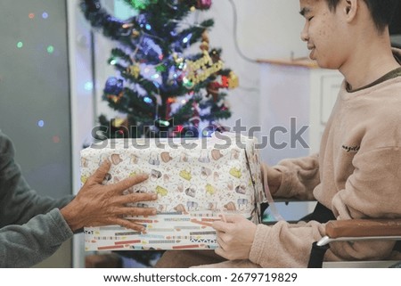 Young man with disability wearing winter pajamas on wheelchair with his father or caretaker in the house with a christmas tree decoration, Holidays and Christmas, Happy New Year with family concept.