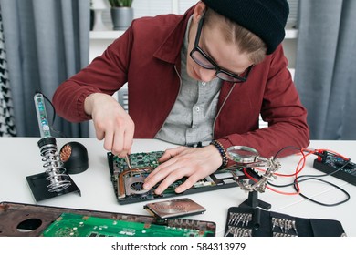 Young man disassembling computer motherboard. Engineer in glasses fixing broken cpu in repair workshop. Electronics development, construction, business concept - Powered by Shutterstock