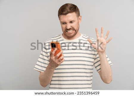 Young man with disgust look at smartphone screen. Portrait of guy cringe and stare with aversion at phone display with squeamishness. Bad awful disgusting awkward joke or inappropriate content. 