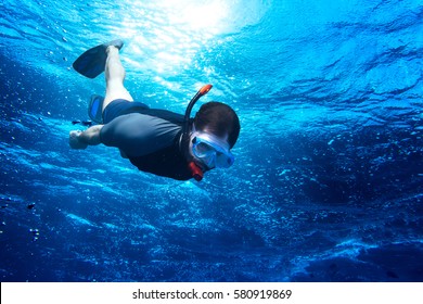 young man diving snorkeling down into the deep blue ocean sea against the sunlight - Powered by Shutterstock