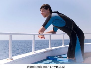 Young Man In Diving Suit Leaning On Boat Fence,looking In To A Sea. Man Wearing Neopren Suit For Water Sports