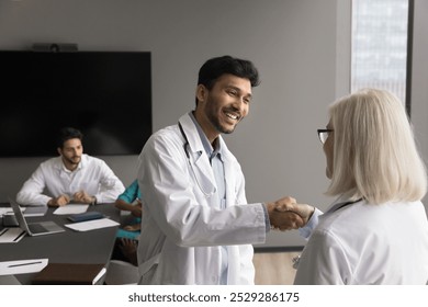 Young man doctor shake hand to senior female teammate feel gratitude for consulting good job help at hard work case. Aged woman cardiologist handshake with grateful intern student younger colleague - Powered by Shutterstock