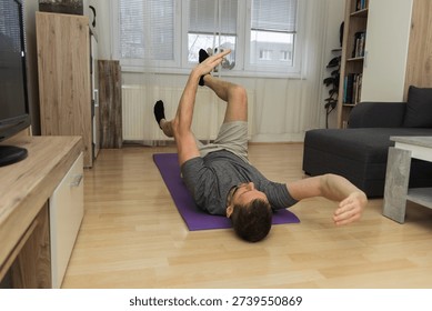 A young man does the dead bug core exercise in his living room to stabilize his spine. Healthy lifestyle, exercising at home