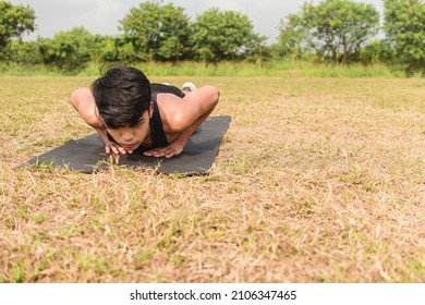 A young man does a set of diamond pushups on a black mat at an open field outdoors. Chest or full body workout.