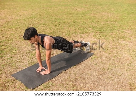 A young man does a set of diamond pushups on a black mat at an open field outdoors. Chest or full body workout.