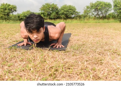 A young man does a set of regular pushups on a black mat at an open field outdoors. Chest or full body workout.