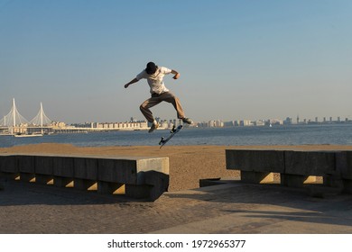 a young man does a trick on a wooden skateboard, in the air, in the setting sun on the street. copyspace. the embankment with sand and lake, clear blue sky