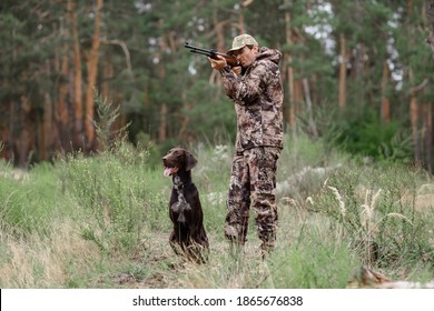 A Young Man With A Dog Came Hunting In The Forest. A Man In Overalls And A Gun Looks Into The Distance. 