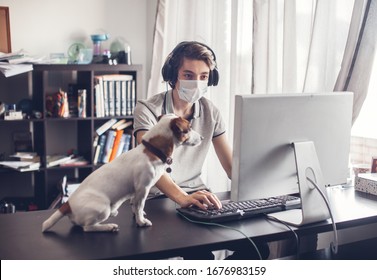 Young Man With Dog In Quarantine. Online Distance Learning. Teen Gaming At Home With Computer, Wearing Protective Mask.