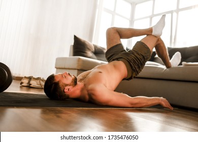 Young Man Doing Abs Exercising At Home On The Couch. Cut View Of Hardwoking T-shirtless Guy Sportsman In Workout Activity At His Apartment. Dumbbells On Pictures Lying On Floor. Trying To Get Better