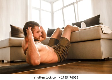 Young Man Doing Abs Exercising At Home On The Couch. Cut View Of Hardwoking T-shirtless Guy Sportsman In Workout Activity At His Apartment. Dumbbells On Pictures Lying On Floor. Trying To Get Better