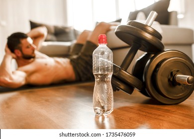 Young Man Doing Abs Exercising At Home On The Couch. Cut View Of Hardwoking T-shirtless Guy Sportsman In Workout Activity At His Apartment. Dumbbells On Pictures Lying On Floor. Trying To Get Better