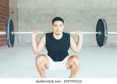 Young man doing barbell squats exercises in a gym. Athletic man training his arms muscles with barbell. Workout in the gym