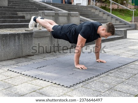 Young man doing a decline push-up or elevated push-up on concrete background outdoors