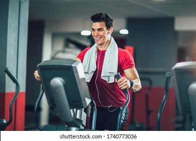 Young man doing exercise on elliptical cross trainer in sport fitness gym club