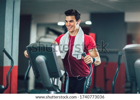 Young man doing exercise on elliptical cross trainer in sport fitness gym club