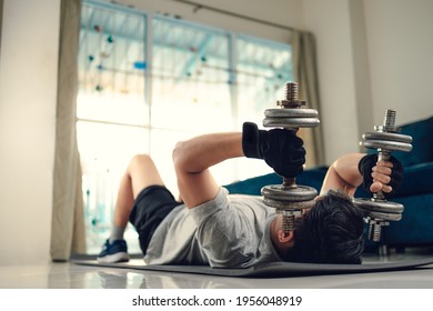 Young Man Doing Exercises Triceps Muscle With Dumbbell On Yoga Mat In Living Room At Home. Fitness, Workout And Traning At Home Concept.