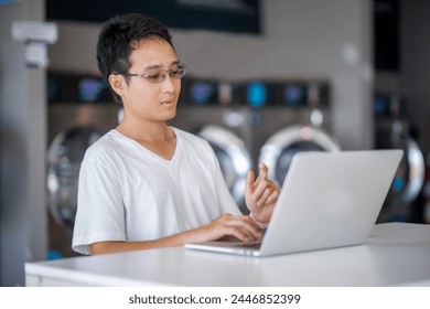 Young Man doing his work, using laptop while waiting for washing machine, Man with his housework and laundry day.