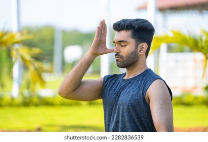 Young man doing nostril breathing or pranayama yoga at park - concept of healthy lifestyle, relaxation and self caring