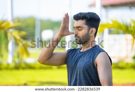 Young man doing nostril breathing or pranayama yoga at park - concept of healthy lifestyle, relaxation and self caring