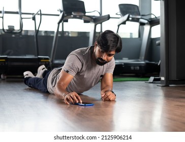 young man doing push ups by setting timer on mobile phone at gym - concept of muscle or bodybuilding, calories tracking and technology.