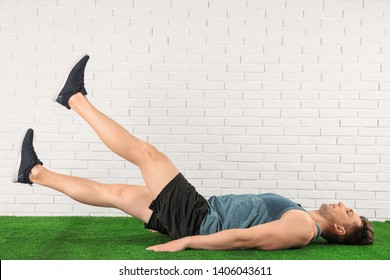 Young man doing scissors exercise on floor near brick wall. Space for text