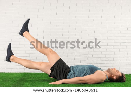 Young man doing scissors exercise on floor near brick wall. Space for text