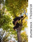 Young man doing a side flip or somersault while practicing parkour on the street with a tree in the background. 