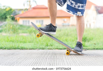 Young Man Doing A Skateboard Trick On A Road In Front Of Home. Skateboarders Feet Close Up.