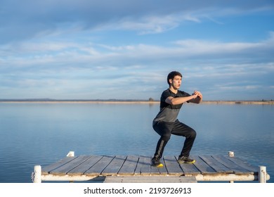 young man doing squats on a lake dock . blue sky - Powered by Shutterstock