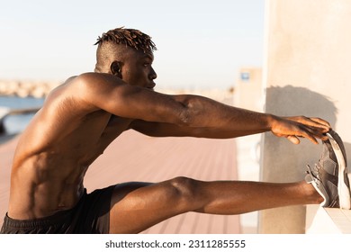 Young man doing stretching exercise outside. African man training at the beach.