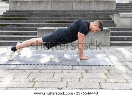 Young man doing a triangle push-up or diamond push-up outdoors on an exercise mat on concrete background. Front view.