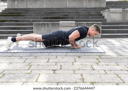 Young man doing a triangle push-up or diamond push-up outdoors on an exercise mat on concrete background. Front view.