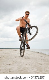 Young Man Doing Wheelie With Bicycle In The Beach