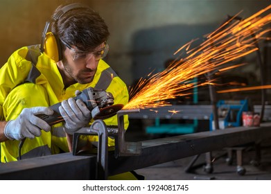 Young man doing work with electric wheel grinding on steel structure in factory
