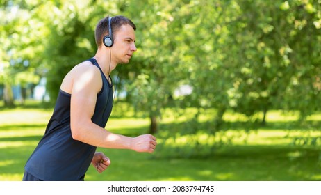 Young Man Doing Workout Outdoor. Muscular Guy Running In The Park, Training, Listening Music In Headphones. Sport, Fitness Healthy Lifestyle Concept. 