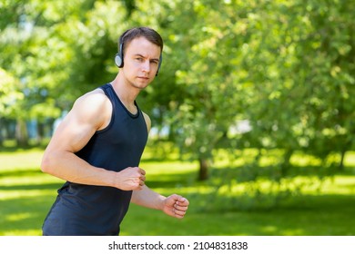 Young Man Doing Workout Outdoor. Muscular Guy Running In The Park, Training, Listening Music In Headphones. Sport, Fitness Healthy Lifestyle Concept.  Copy Space