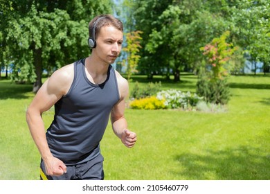 Young Man Doing Workout Outdoor. Muscular Guy Running In The Park, Training, Listening Music In Headphones. Sport, Fitness Healthy Lifestyle Concept.  Copy Space