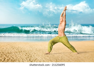 Young man doing yoga and meditating in warrior pose on beach
