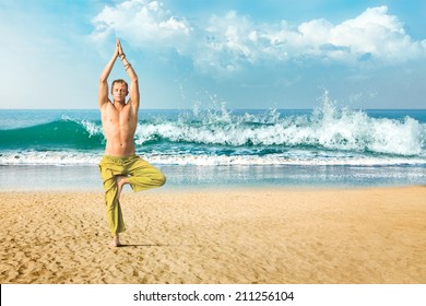 Young man doing yoga and meditating in tree position at sea beach