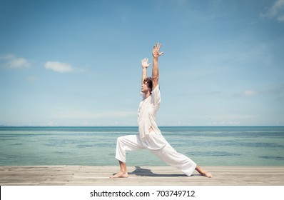 Young Man Doing Yoga Warrior Pose On A Beautiful Tropical Beach