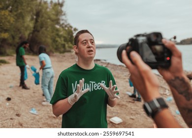 Young man with down syndrome wearing a volunteer t-shirt and gloves is being interviewed by a videographer during a river cleanup - Powered by Shutterstock