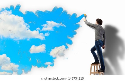 Young Man Drawing A Cloudy Blue Sky On The Wall