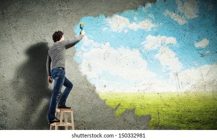 Young man drawing a cloudy blue sky on the wall